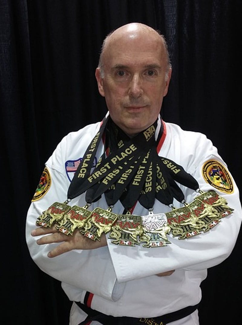 Michael Busha in his karate gi, arms crossed, wearing a row of tournament medals